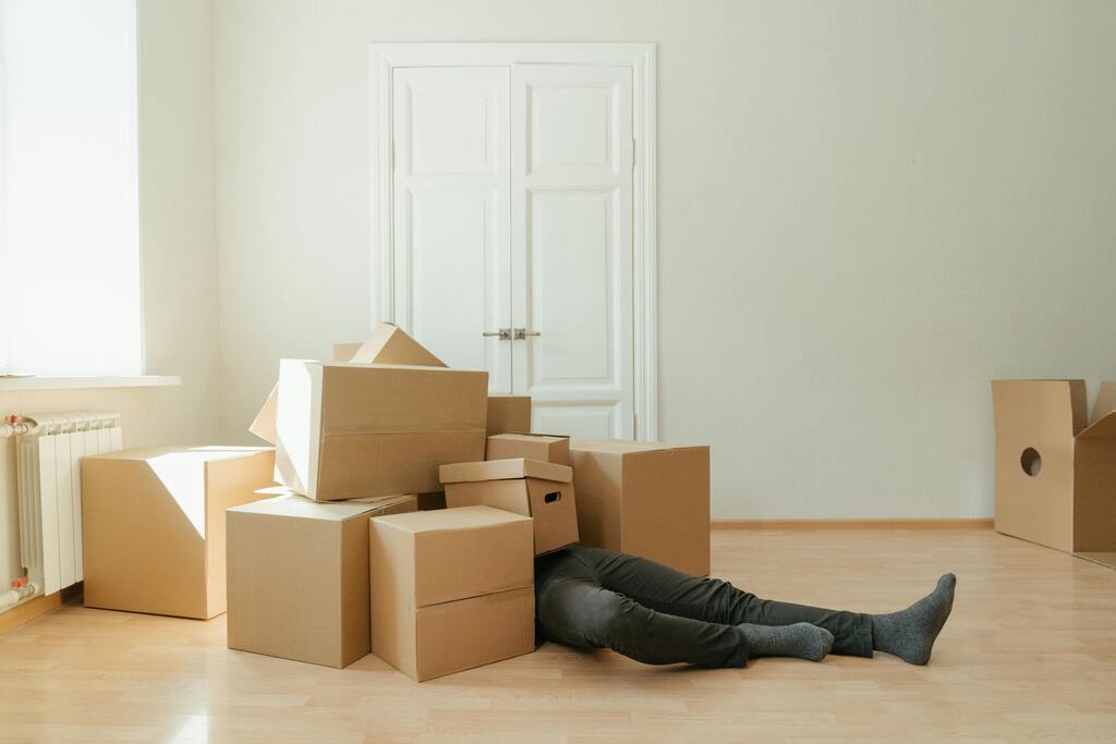 Person on floor surrounded by cardboard boxes during moving; concept of stress and relocation.